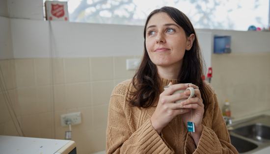 A young woman contently sips her tea in warm comfotable accommodation.